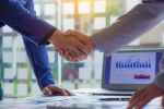 businesspeople shaking hands at a meeting in modern office Success concept of teamwork, collaboration and a handshake on the table with graph paper and laptop with orange light.