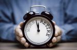 Businessman holding black alarm clock with clockwise countdown from work to retirement.